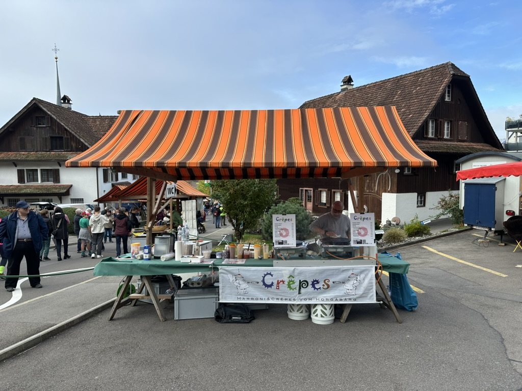 Unser Marktstand mit orange-braun gestreiftem Sonnendach an einem Dorfmarkt